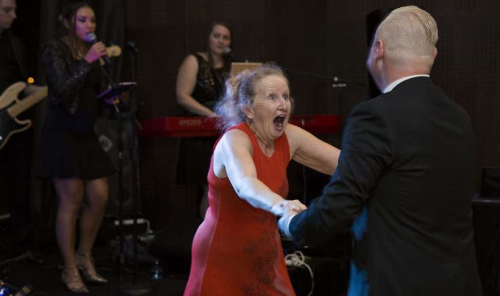A dancer in a red dress laughing with her partner in front of a live band